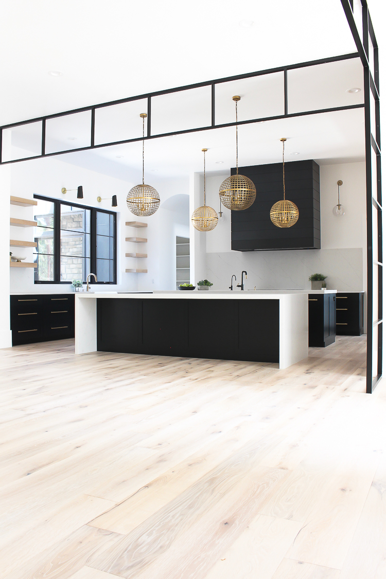 A modern black kitchen with brass accents and open shelving. 